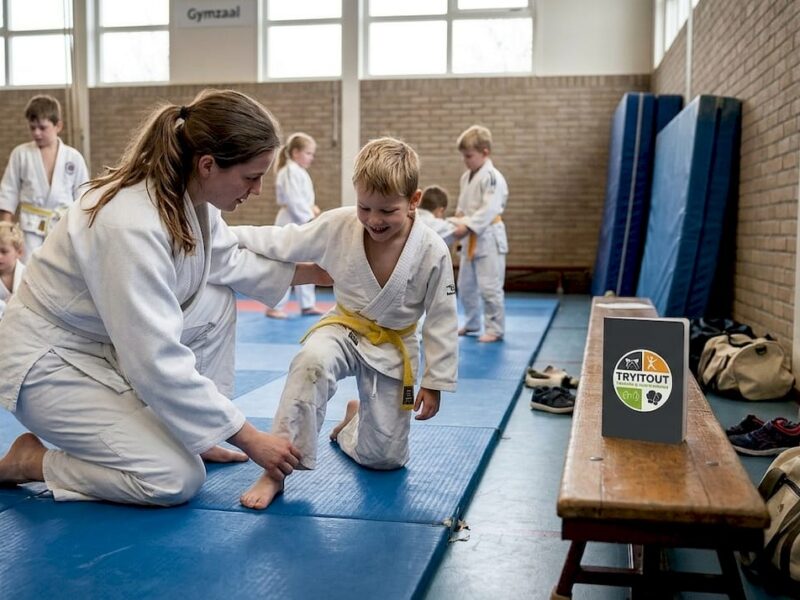 In de sportzaal zijn kinderen enthousiast bezig met judotraining onder begeleiding van hun trainer.