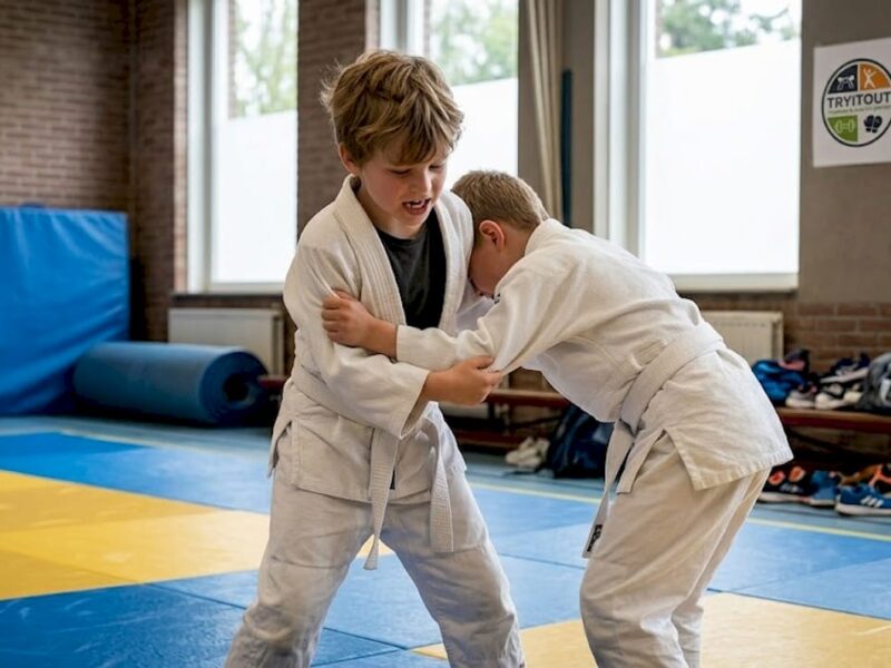 In de gymzaal werken kinderen enthousiast aan het verbeteren van hun judotechnieken.