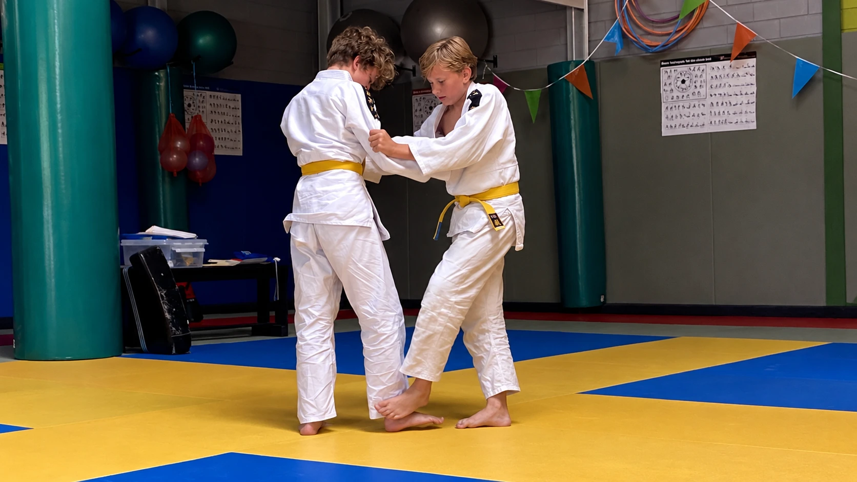 Twee jeugdjudoka's oefenen grip en balans onder begeleiding van de trainer.