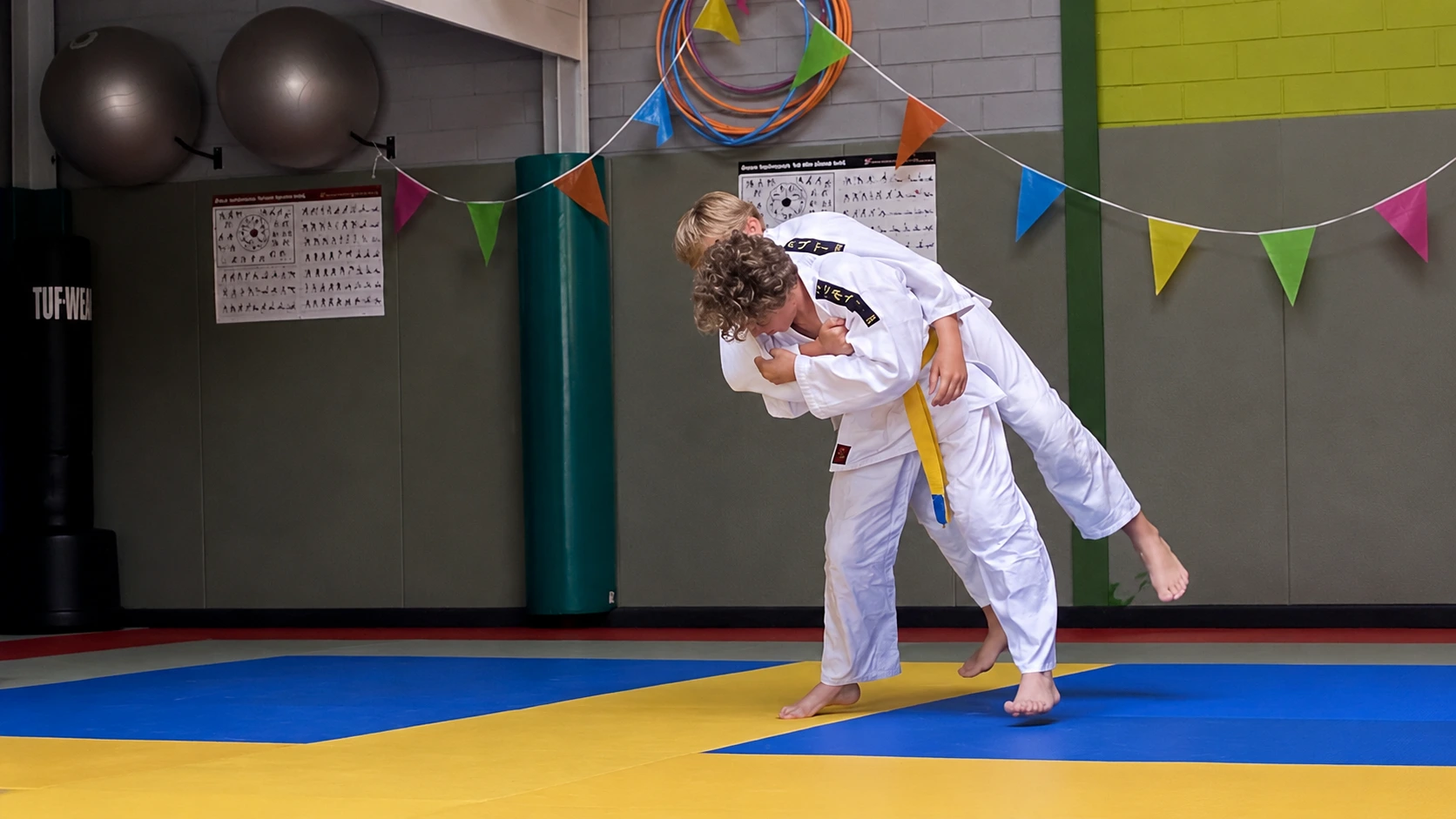 Twee jeugdjudoka's oefenen samen een gecontroleerde judoworp.