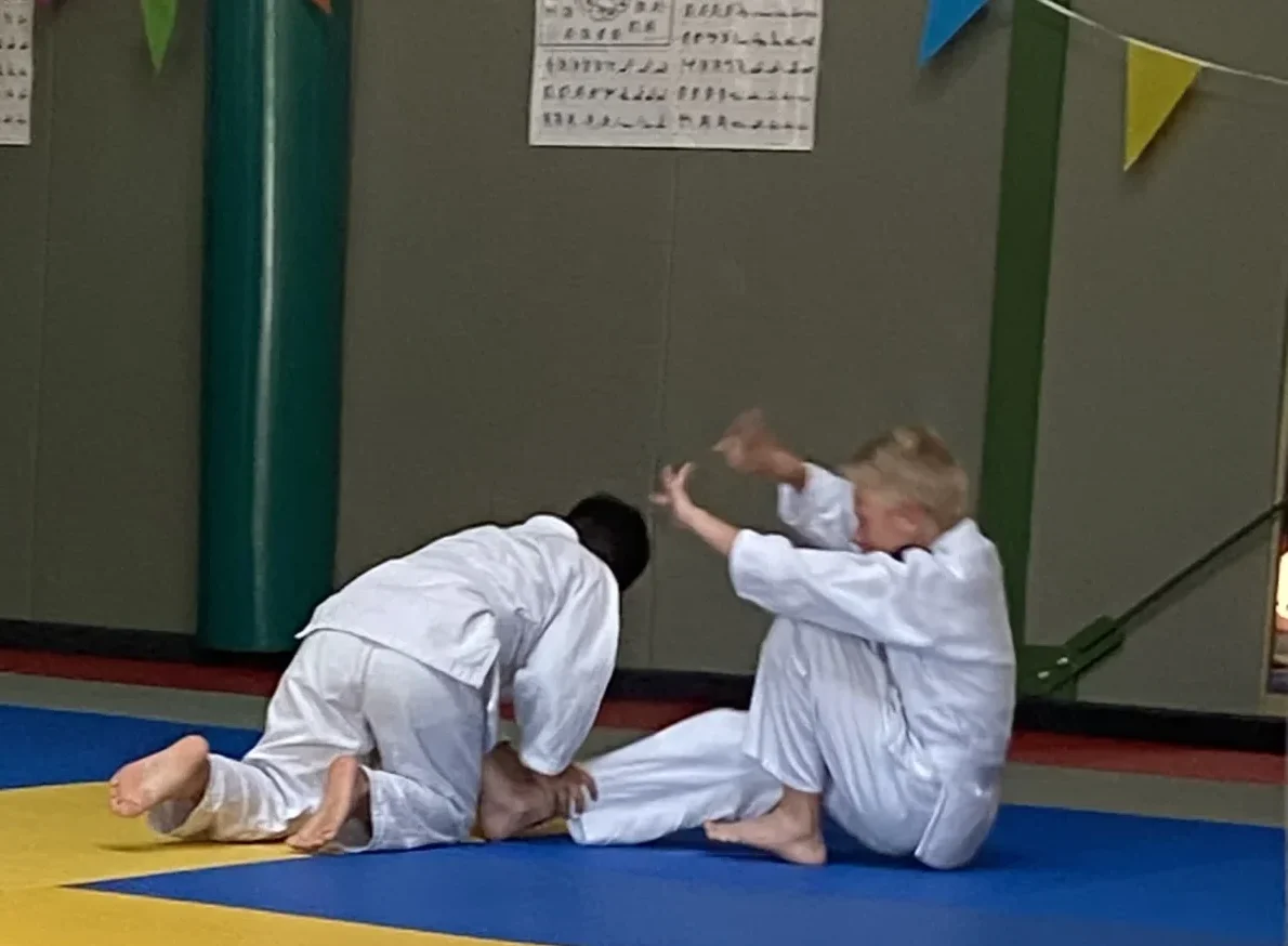 Kinderen leren veilige jujutsu technieken en valbreken tijdens de jeugdtraining
