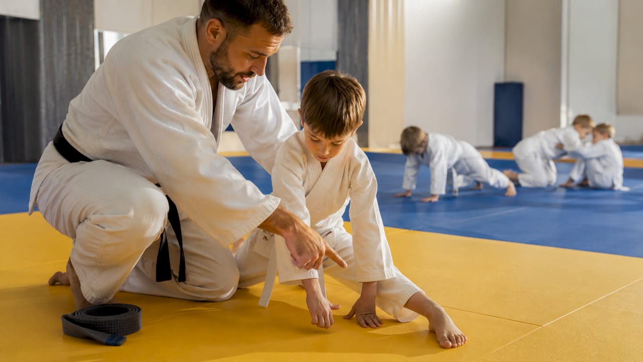 Trainer legt de judotechniek rustig uit aan het kind